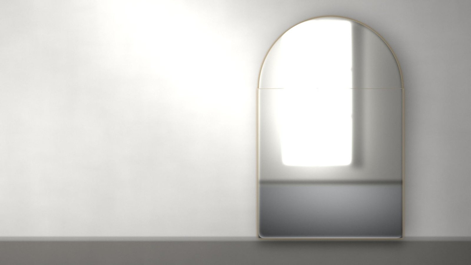 A tall arched mirror standing against a plaster wall, its bevelled edge catching low daylight and its face carrying the reflection of a window and floor.