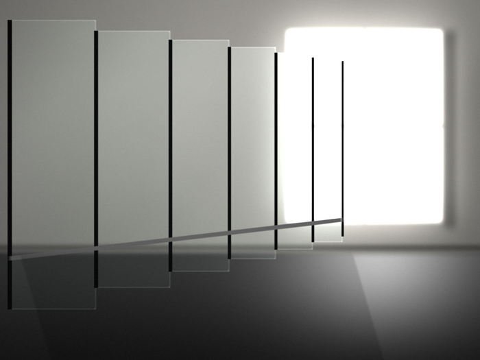 A run of glass office screens receding towards a bright window, dark posts between the panels and light pooling on the floor.
