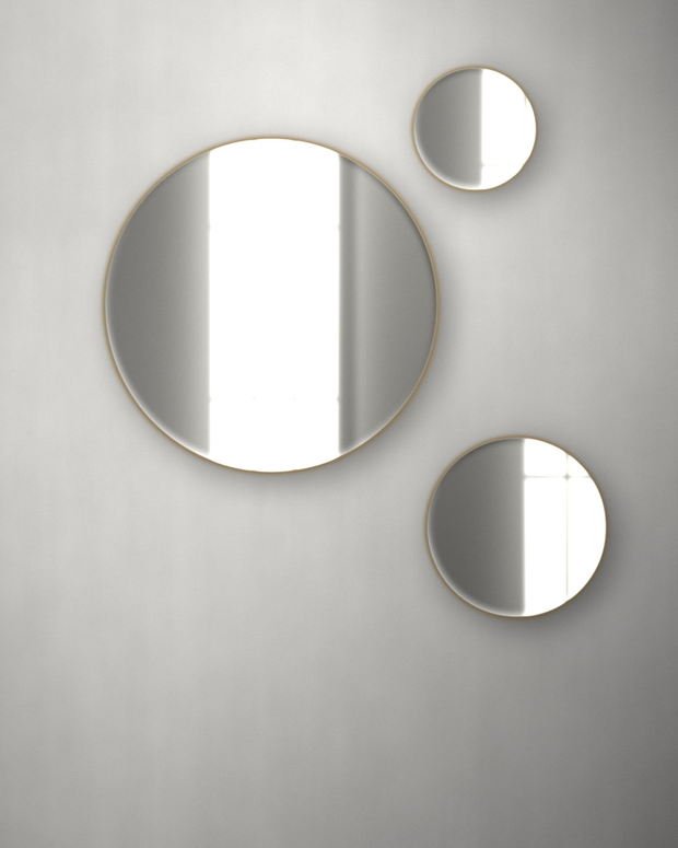 Three round brass-edged mirrors hung as a cluster on a plaster wall, each holding a different part of the daylight.